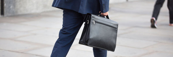 Man in a suit walking with a black leather briefcase on a city sidewalk, featured as the cover photo for a Leather Briefcase Buying Guide.