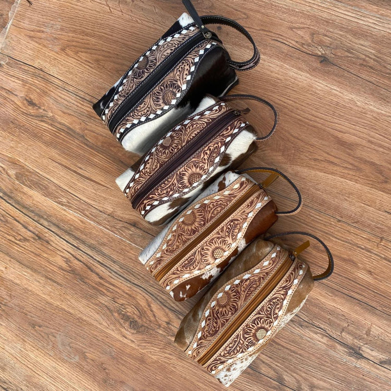 Collection of four Western Luxe Leather Toiletry Bags in various styles: Golden Cowhide, Midnight Cowhide, Jet Black, and Rich Mahogany, each featuring unique hand-tooled detailing.