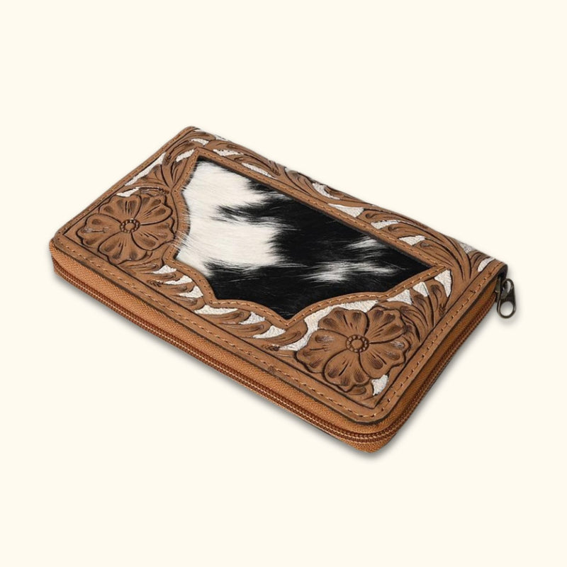 Angled view of handcrafted Western leather cowhide clutch with intricate floral tooling and hair-on hide accent.