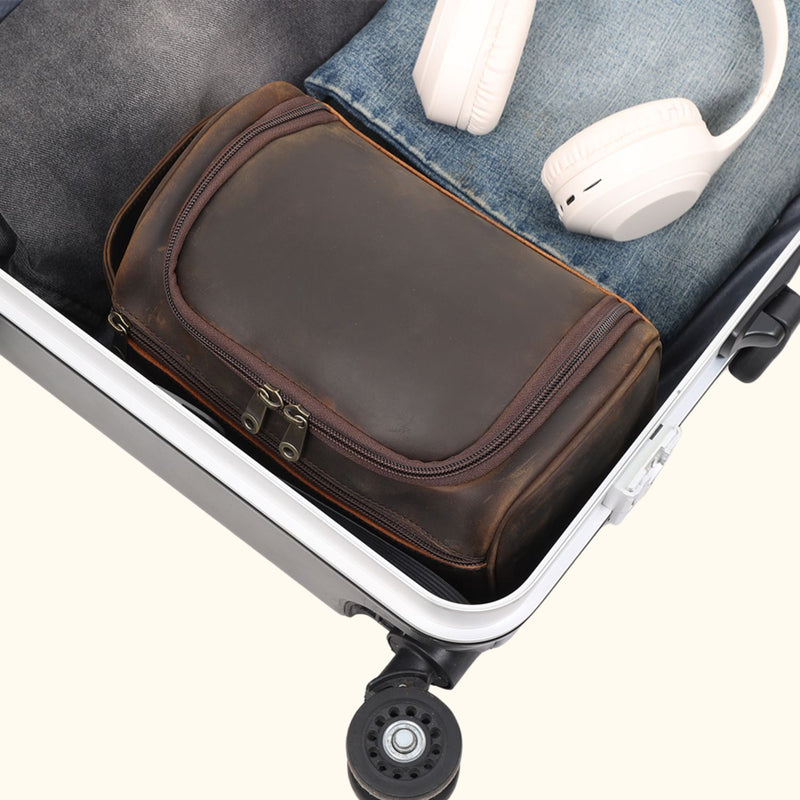 The High Plains Leather Toiletry Bag neatly fits in a suitcase, highlighting its compact, next to headphones and clothing, ready for travel.