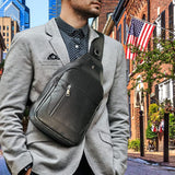 Man wearing a Western Adventure Leather Sling Bag across his chest, standing in an urban setting with buildings and an American flag in the background.