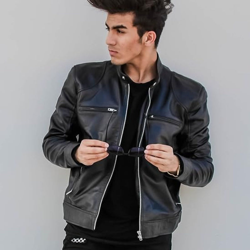 Man wearing a black leather jacket and holding sunglasses, looking to the side.