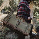 The Weekender - Waxed Green Canvas Leather Duffel being carried by a man in a plaid shirt, showcasing its rugged, durable design perfect for outdoor adventures.